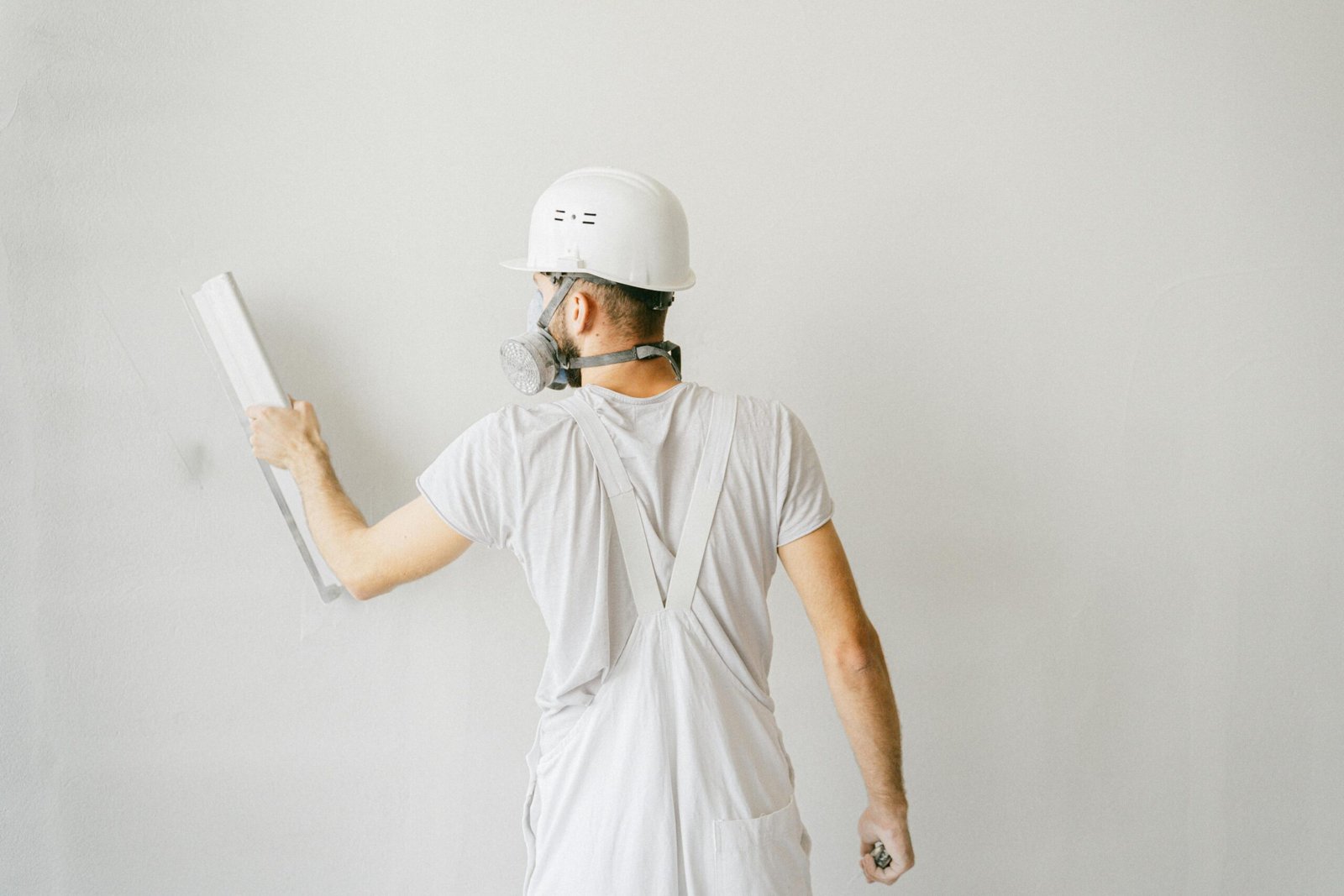 Services Back view of a construction worker in safety gear plastering a white wall.